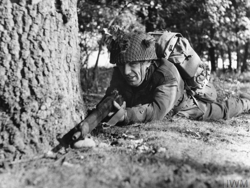 A paratrooper on exercise takes cover by a tree