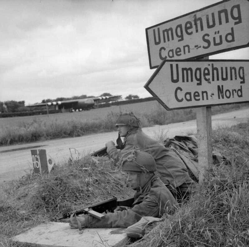 Airborne soldiers dug in next to a German signpost in Normandy