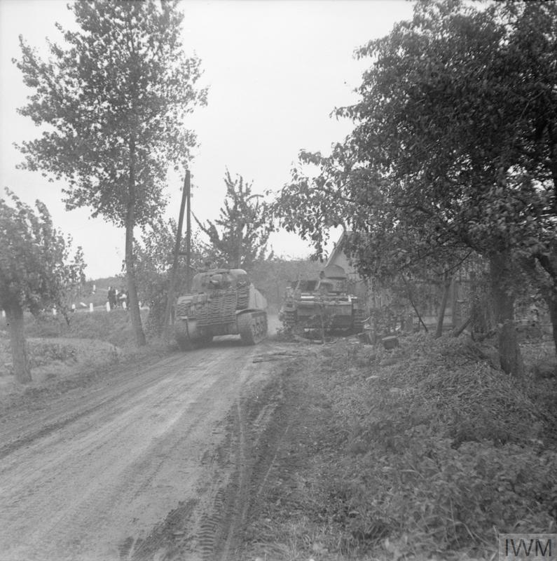 A Sherman tank passes a knocked-out German tank